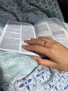 a woman's hand holding an open book on top of a bed with blue and white sheets