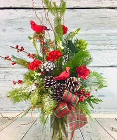 a vase filled with red flowers and pine cones