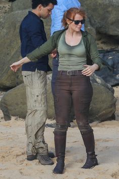 a woman standing on top of a sandy beach next to a man in blue shirt and brown pants