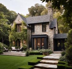 a stone house with steps leading up to the front door and patio area, surrounded by lush greenery