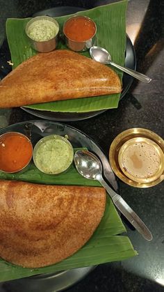 two plates filled with food on top of a green leaf covered table next to silver spoons