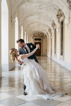 a bride and groom dance in an ornate hallway at their wedding reception, the bride is wearing a flowing white dress