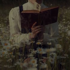 a woman is sitting in the grass reading a book with daisies all around her