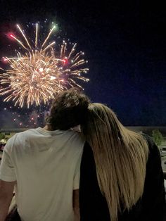 two people standing next to each other with fireworks in the background