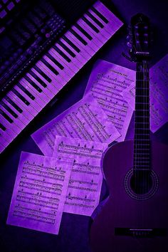 an acoustic guitar sitting next to sheet music and piano keys in front of purple lighting