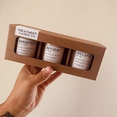 a hand holding an open cardboard box with three candles in it that are labeled'treatment candle co '