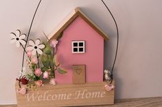 a small pink house with flowers in the front and welcome home sign on the back