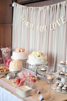 a table topped with lots of cakes and cupcakes next to a sign that says hooray for love