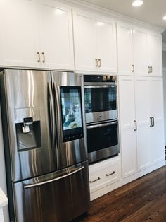 a stainless steel refrigerator and oven in a kitchen with white cabinets, wood flooring and hardwood floors