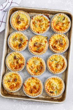 twelve mini quiche pies on a baking sheet ready to go into the oven