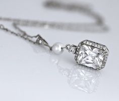 Classically elegant and sophisticated! Emilia cz crystal bridal necklace made in a radiant cut with a frame of tiny cz crystals for a beautiful sparkling accessory that will suit your dress, whatever style. The 18K rhodium setting has delicate carving around the sides so your necklace is pretty from all aspects!A Swarovski pearl in your custom color adds a personalized touch your Emilia necklace.Measures: 2" (5 cm) top to bottom. 0.5" (1.2cm) widest point.All components are  rhodium plated sterl White Gold Rectangular Pendant For Wedding, Elegant Rectangular Pendant Necklace For Wedding, Elegant Rectangular Pendant Jewelry For Wedding, Elegant Radiant Cut Jewelry For Weddings, Elegant Rectangular Necklaces For Wedding, Rectangular White Gold Necklace For Wedding, White Gold Rectangular Wedding Necklace, Elegant Rectangular Wedding Necklaces, Classic Wedding Jewelry With Rectangular Pendant