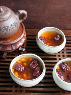 three white bowls filled with soup next to a tea pot and wooden grate on top of a table