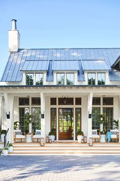 a white house with lots of windows and plants on the front porch, surrounded by brick pavers