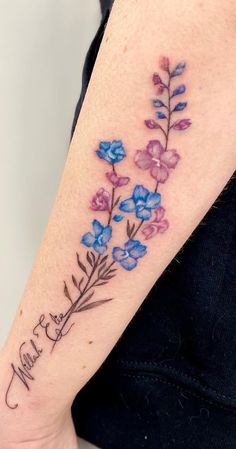 a woman's arm with blue and purple flowers on the left side of her arm