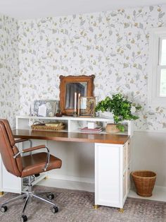 a desk with a chair, mirror and potted plant on it in front of a wallpapered wall