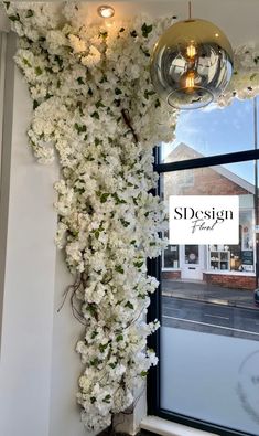 white flowers are growing up the side of a window in front of a storefront