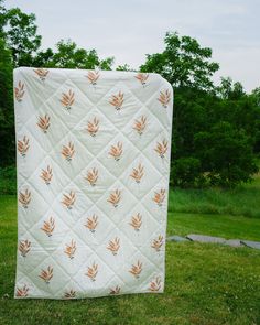 an orange and white quilt sitting on top of a green grass covered field with trees in the background