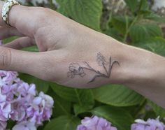 a woman's hand with a flower tattoo on her left wrist and purple flowers in the background