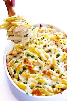 a wooden spoon scooping some pasta from a casserole dish with chicken and cheese