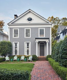 a large gray house sitting on top of a lush green field next to a brick walkway