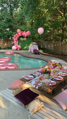 an outdoor pool party with pink balloons and plates on the table next to the pool