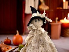 a cloth doll with a black hat and white dress sitting in front of some pumpkins