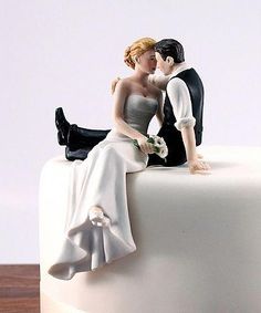 a bride and groom figurine sitting on top of a white wedding cake together