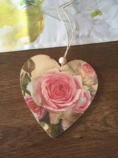 a heart shaped ornament with a pink rose on it sitting on a table