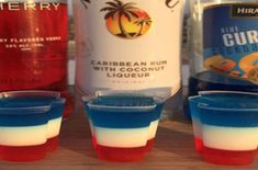 three glasses filled with red, white and blue liquid next to two bottles of vodka