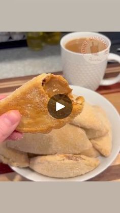 a person holding a piece of bread in front of a cup of coffee on a table