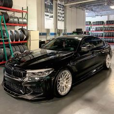 a black car parked in a garage next to some shelves with tires on the wall