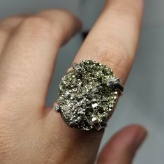 "Make a statement and give the gift of strength with our Raw Pyrite Ring. This exquisite piece showcases the bold beauty of pyrite, known for its metallic luster and protective energy. It's more than a statement piece; it's a meaningful gift that captures the essence of confidence and resilience. 🔸 Adjustable band ring 🔸25mm stone size 🔸Color may vary according to lighting 🔸Silver filled We offer  🔸Fast shipping ( under normal conditions) 🔸Free shipping  🔸Polishing cloth ( to keep your piece shiny) 🔸Jewelry case on orders of 100€ 🔸Gift box 🎁 🔸Great customer service                                 Pyrite, often called \"Fool's Gold,\" is cherished for its reflective qualities and is believed to shield against negative energy and draw money closer to you. Its captivating shine mak Spiritual Raw Stone Rings For Anniversary, Raw Stone Ring For Anniversary, Anniversary Raw Stone Ring Jewelry, Gold Ring With Raw Stone For Healing, Unique Rings With Raw Stone For Gift, Spiritual Crystal Ring With Raw Stone For Gifting, Spiritual Raw Stone Crystal Ring Gift, Gold Jewelry With Raw Stone For Promise Ring, Gift Crystal Open Ring With Raw Stone