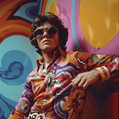 a man wearing sunglasses sitting in front of a colorful wall