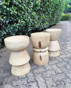 three wooden stools sitting next to each other on a sidewalk in front of bushes