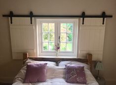 a bed with white sheets and purple pillows in front of a window that looks out onto the yard