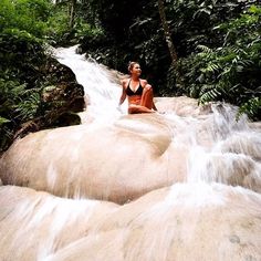 a woman sitting on top of a rock next to a waterfall in the jungles