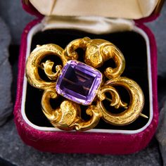 This fabulous brooch features a light purple cushion cut amethyst set into a flourished setting with engraved floral details. The purple color and the unpolished yellow gold complement each other beautifully. The pin is crafted in 10k yellow gold and is complete with a 14k gold C-clasp closure. Lavender Brooch Jewelry As A Gift, Elegant Purple Gemstone Brooches, Elegant Intaglio Brooches For Gifts, Victorian Yellow Gold Brooches With Gemstone, Purple Amethyst Gemstone Brooches, Purple Gemstone Brooches For Gift, Elegant Amethyst Brooches For Wedding, Antique Yellow Gold Brooches With Gemstone, Antique Hallmarked Purple Brooches