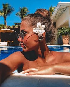 a woman wearing sunglasses and a flower in her hair sitting by the edge of a swimming pool