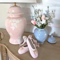 a pink vase with flowers and ballet shoes on a table next to a blue vase