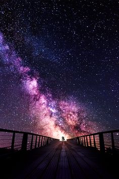 two people standing on a bridge looking up at the night sky with stars in the background