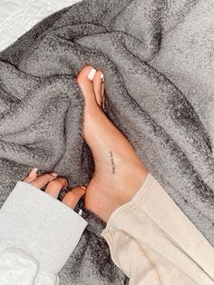 a woman's bare feet with tattoos on her left leg and right foot resting on a gray blanket