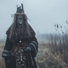 a person with long hair and makeup standing in the middle of a field wearing an elaborate costume