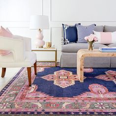 a living room filled with furniture and pillows on top of a blue rug in front of a white wall