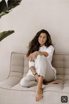 a woman sitting on top of a couch next to a plant