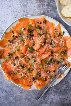 a white plate topped with salmon and olives next to slices of bread on top of a table