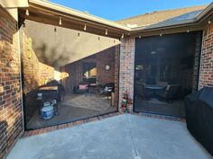 an open garage door in front of a brick building with patio furniture and bbq