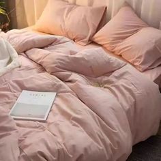 a pink comforter on a bed next to a vase with flowers and a book