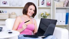 a woman sitting on a white couch holding a credit card and a laptop in her lap