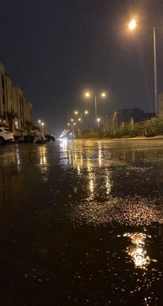 cars parked on the side of a wet street at night with lights reflecting off the wet pavement