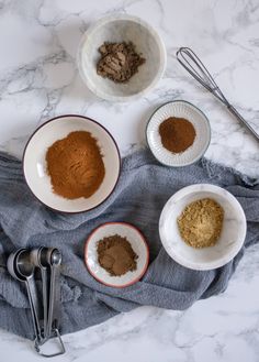 three bowls filled with spices on top of a table next to utensils and spoons